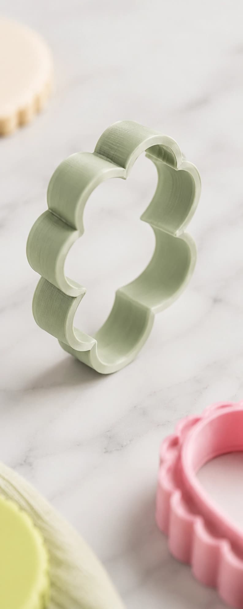 A pale green flower-shaped printed cutter, standing on a studio worktop