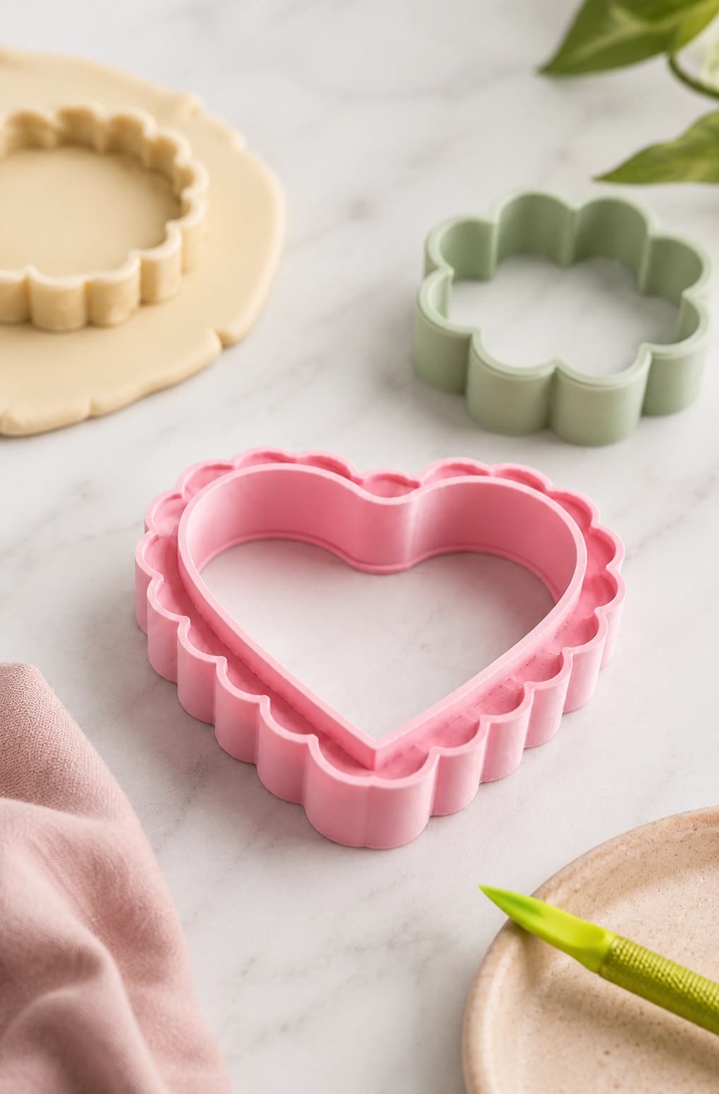 Pink heart cookie cutter with green and cream floral cutters on a light worktable